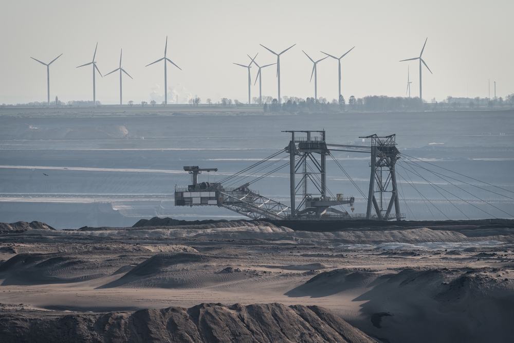 A picture of a mine site with a large crane and wind turbines in the backgound