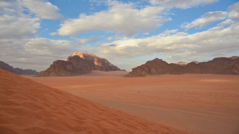 A flat desert landscape with mountains in the background under blue sky and clouds